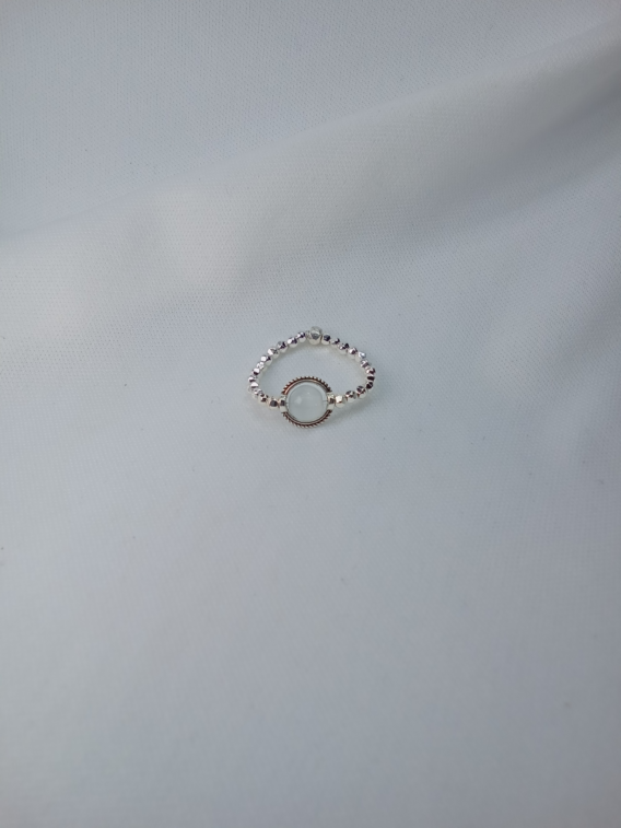 Bague en pierre naturelle pour femme. Un pierre au centre du bijou sertie d'un cercle ciselé. Le tour de la bague est constituée avec des perles effet diamanté en acier inoxydable. Créée en Moselle dans l'est de la France.