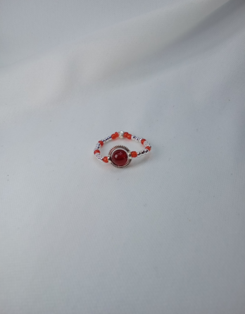 Bague artisanale créé en Moselle dans l'est de la France. La bague Orlyane est conçue avec une pierre d'agate rouge sertie dans un cercle ciselé en acier inoxydable. Des perles de verres et argenté entourent la bague de couleurs rouge et argenté.