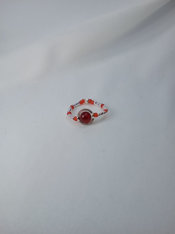 Bague artisanale créé en Moselle dans l'est de la France. La bague Orlyane est conçue avec une pierre d'agate rouge sertie dans un cercle ciselé en acier inoxydable. Des perles de verres et argenté entourent la bague de couleurs rouge et argenté.