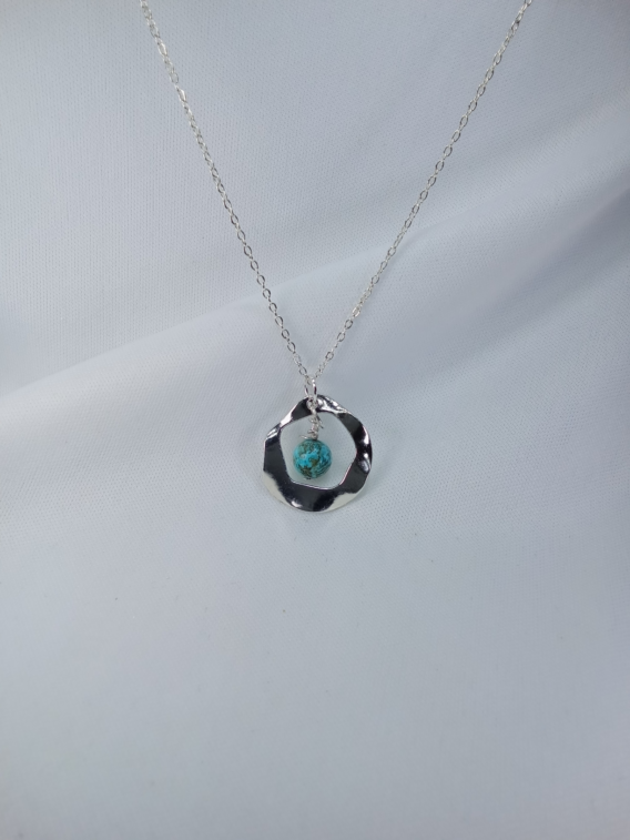 Collier en argent pour femme avec un pendentif rond bosselé qui capture une pierre naturelle de turquoise. Bijou crée près de Metz.